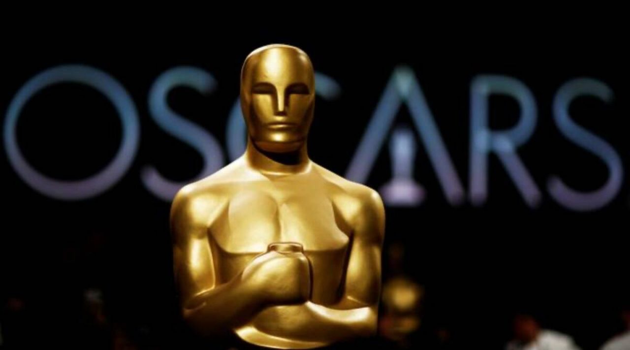 A statue of the Oscars is standing in front of the word 'oscars'